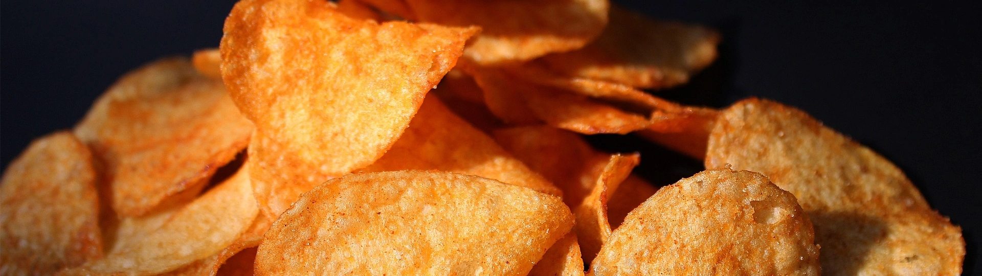 Kartoffelchips – Knuspriger Snack für jeden Anlass Goldbraune, knusprige Kartoffelchips auf schwarzem Untergrund verteilt – der perfekte Snack für gesellige Momente und puren Genuss.