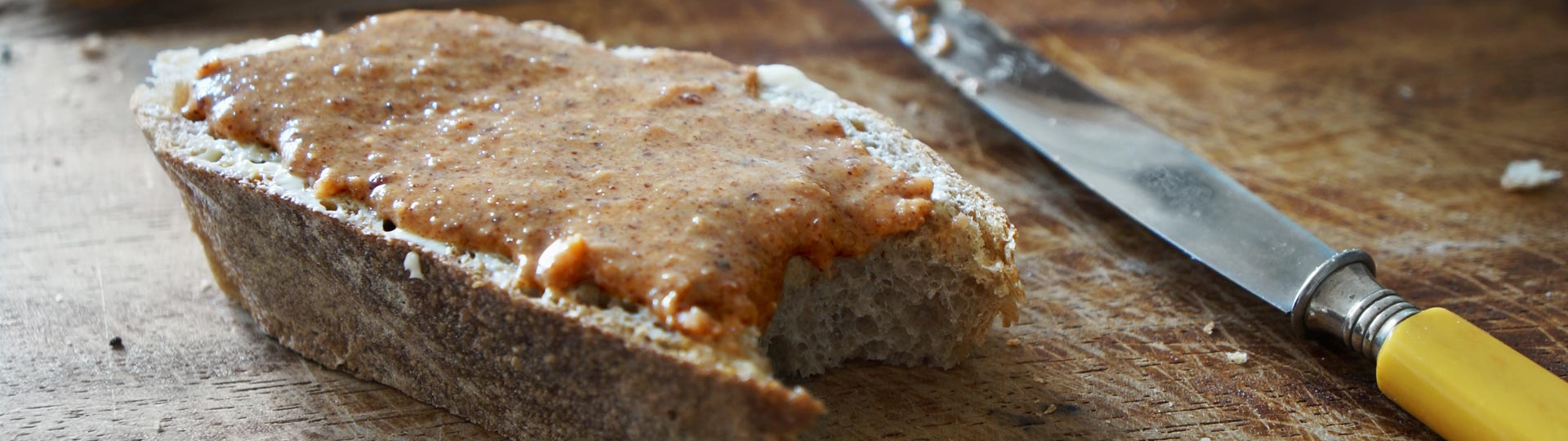 Brandgut Kategorie Marke Kategorie-Bild: eine Scheibe dick geschnittenes Brot mit Brandgut Nussaufstrich auf einem rustikalen Holzbrettchen