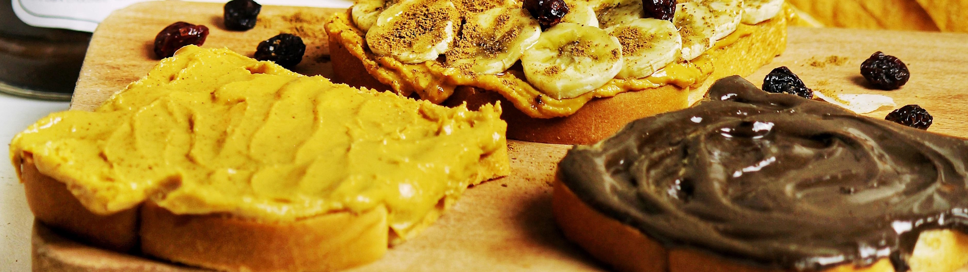 Erdnussbutter-Brote mit Bananen und Schoko-Nusscreme Brotscheiben mit cremiger Erdnussbutter bestrichen, teils belegt mit Bananenscheiben und teils verfeinert mit Schoko-Nusscreme, appetitlich angerichtet auf einem rustikalen Holztisch.